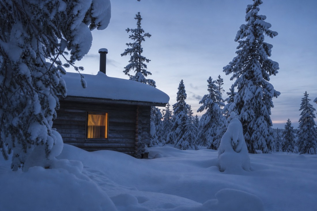 A snow-covered wooden cabin among spruce trees in Finnish Lapland