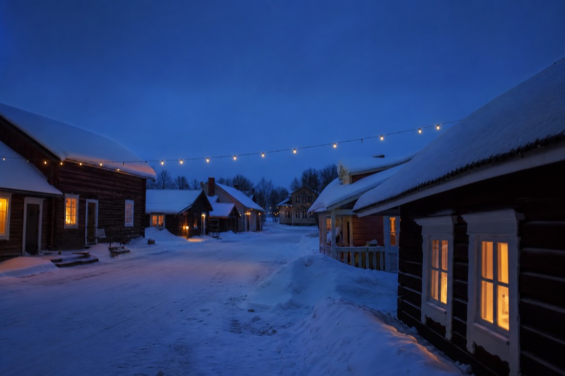 A snowy Nordic village street at dusk with warm lit windows