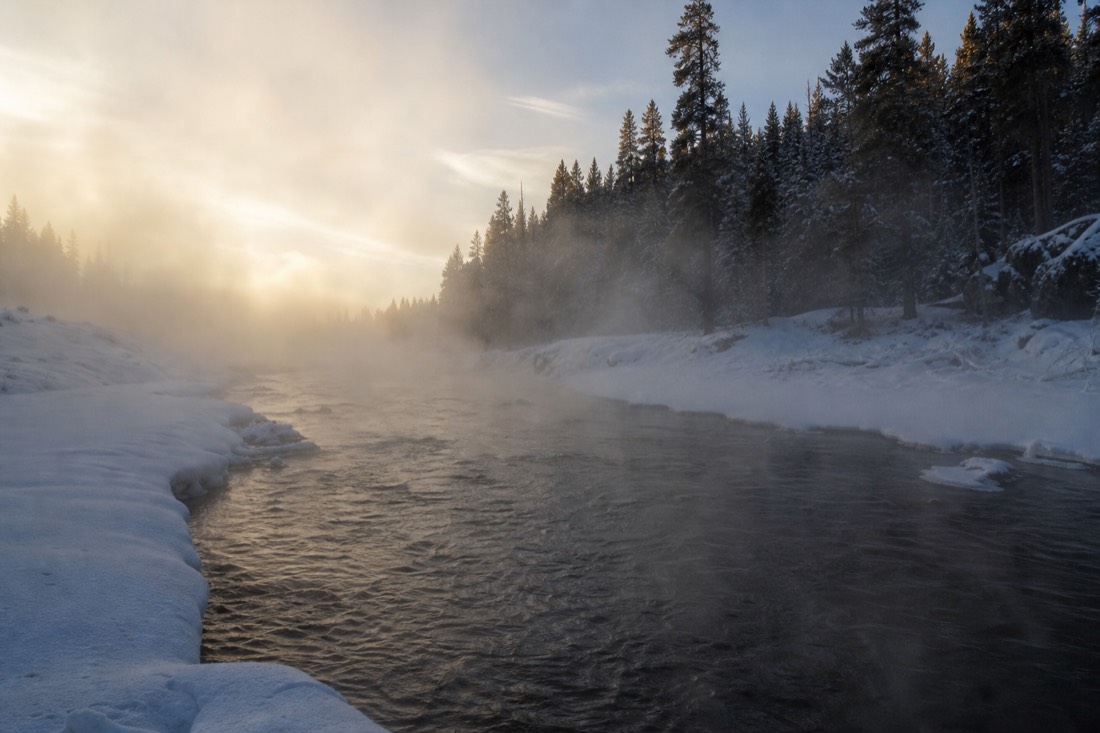 Steam rising off an open stretch of river in deep winter, snowbanks either side